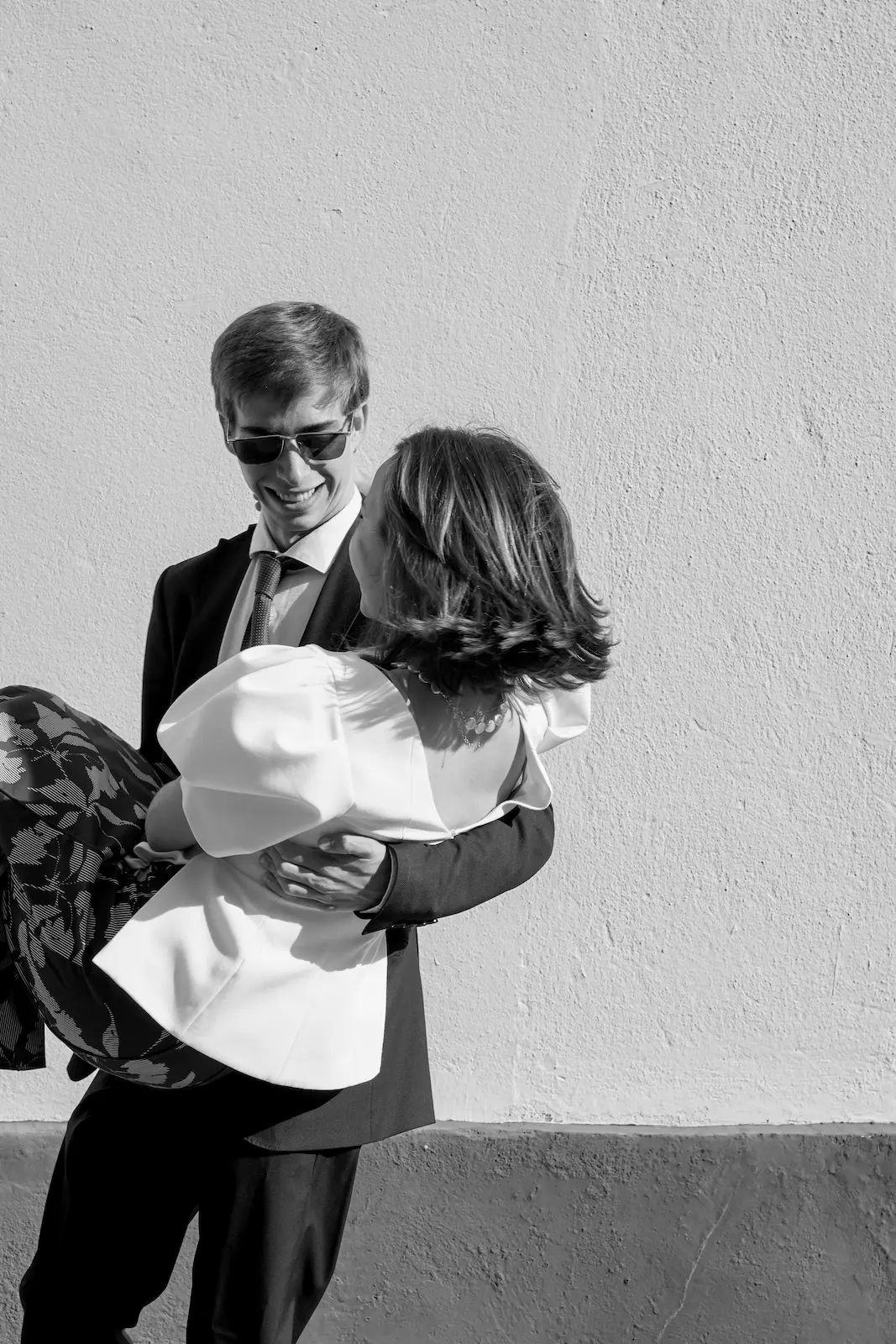 Pareja de novios abrazándose junto a una pared blanca, fotografía de boda en blanco y negro