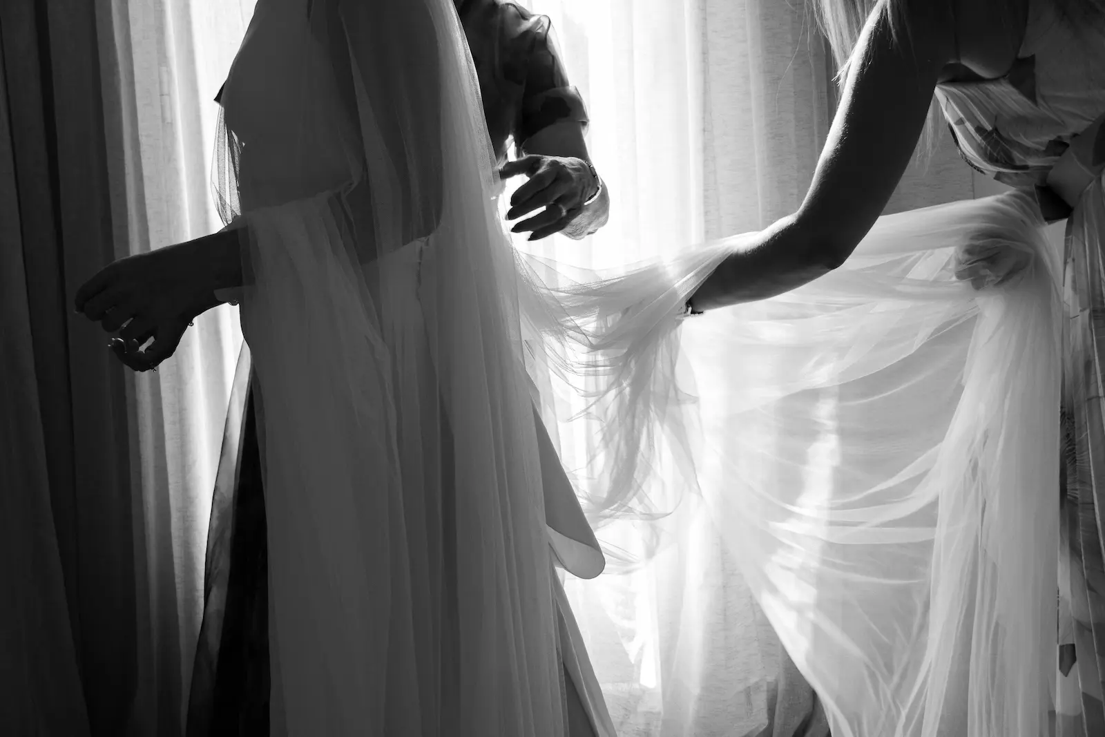 Detalle del vestido de novia con velo mientras la ayudan a vestirse, fotografía documental de boda