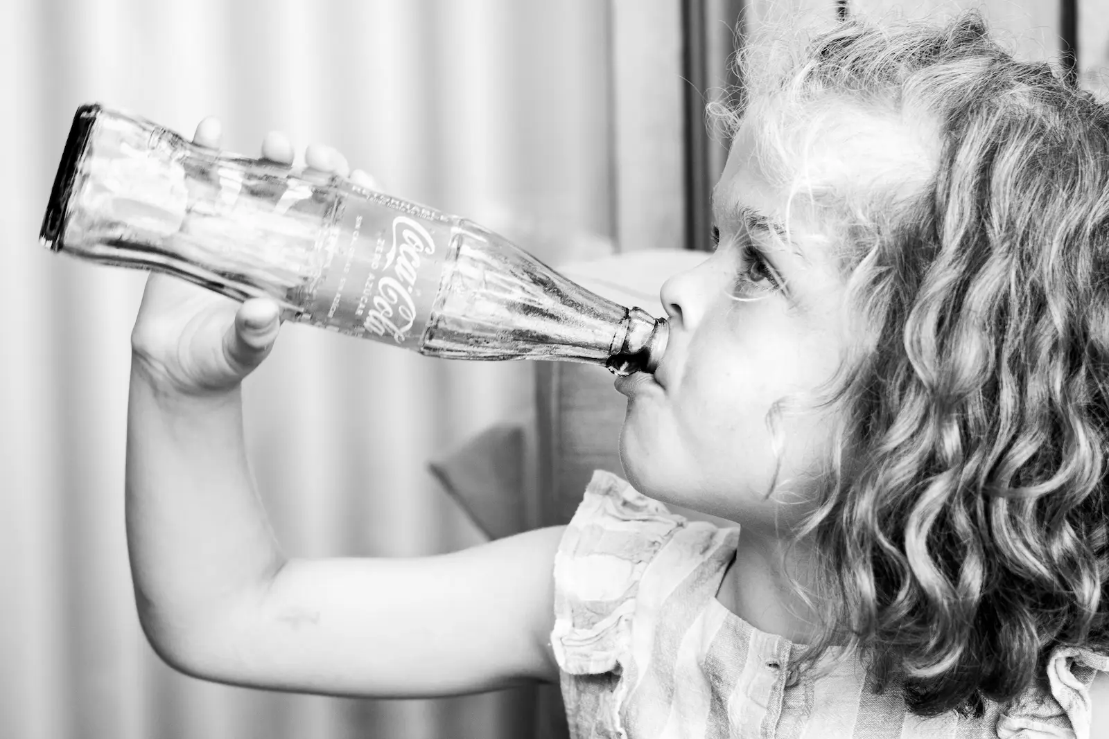 Niña con pelo rizado bebiendo de una botella de cristal en una boda, retrato infantil en blanco y negro