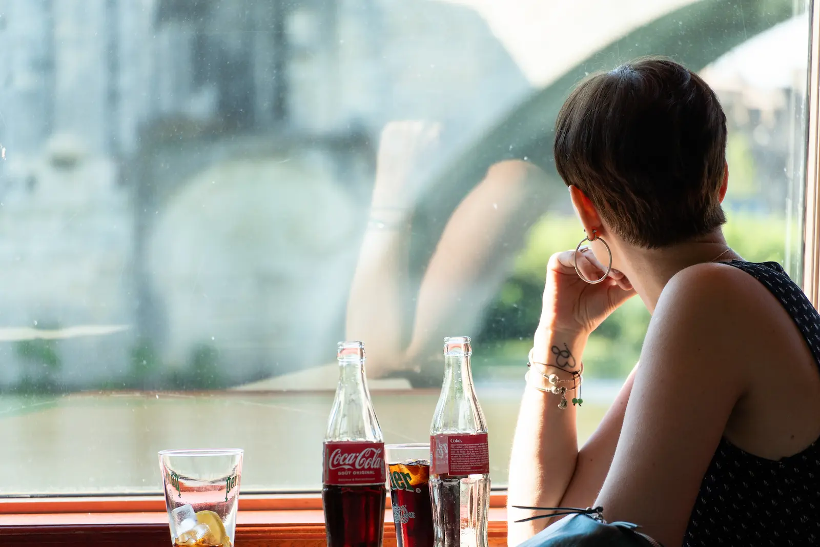 Mujer de espaldas mirando por la ventana de un café con luz natural, fotografía de retrato en color