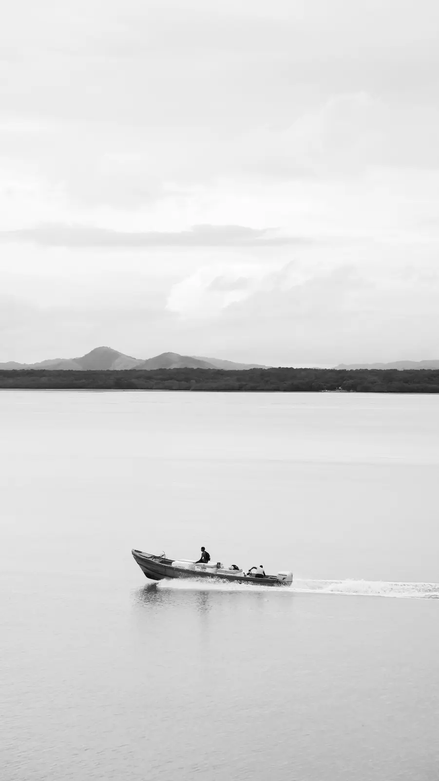 Barca de pesca cruzando una bahía tranquila con montañas al fondo, fotografía minimalista en blanco y negro