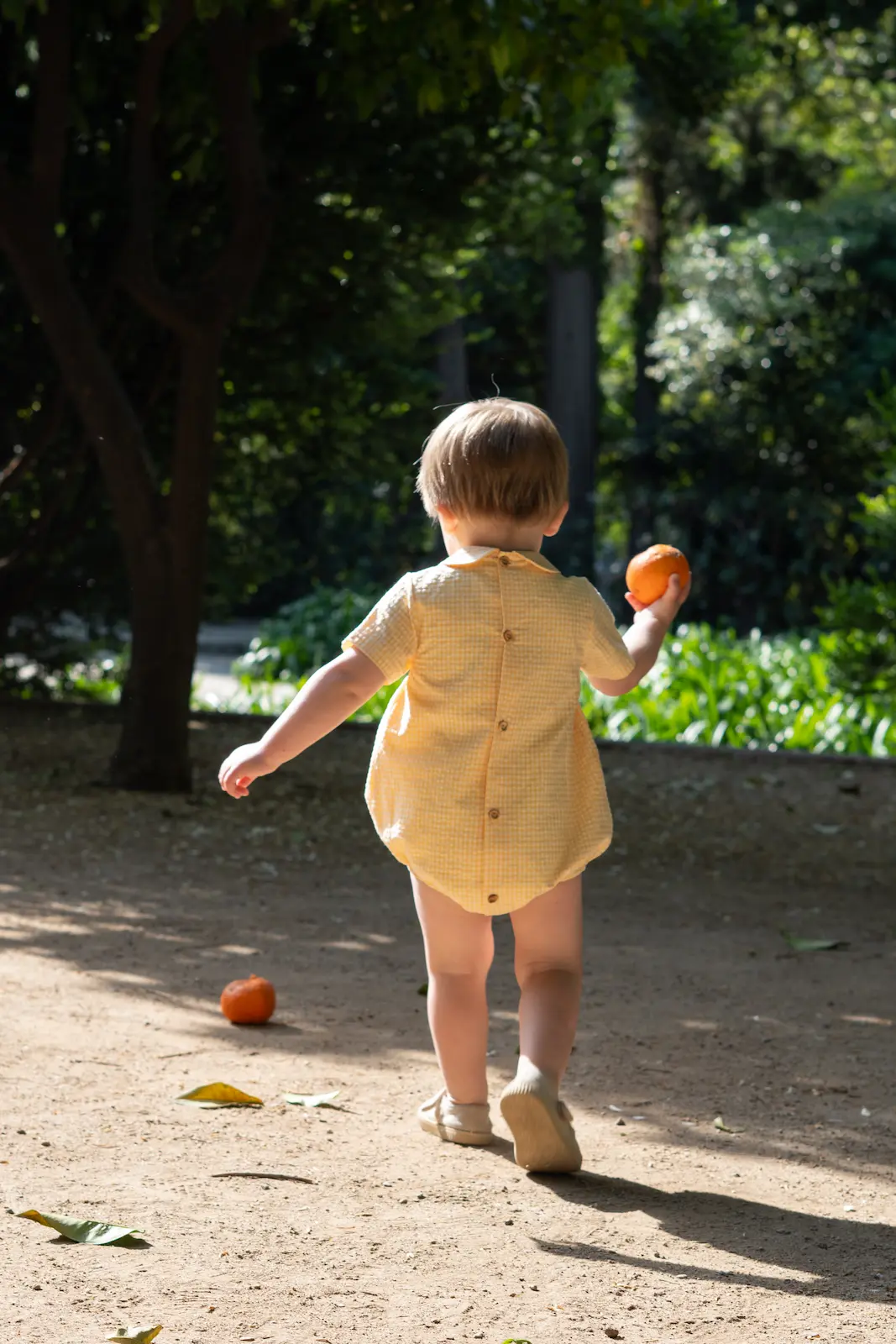 Bebé de espaldas caminando en un jardín con luz de verano, fotografía de familia al natural